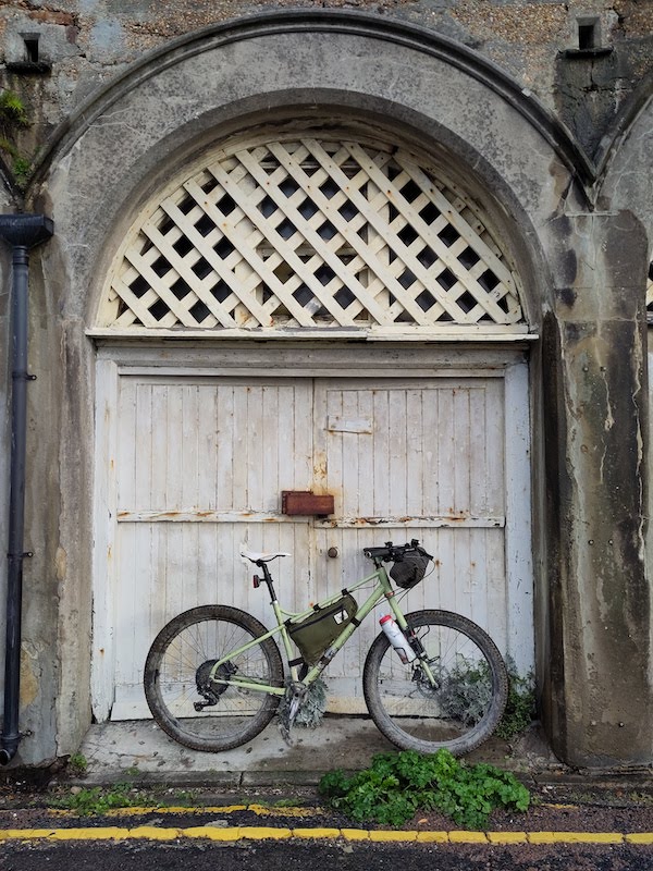 A mountain bike resting against a sea-weathered dilapidated wooden door to an under-arch building on Brighton seafront.