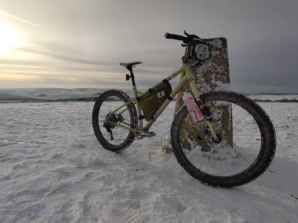 A mountain bike in the foreground, the snow-covered South Downs Park in the background with the sun breaking through the fuzzy cloudy sky.