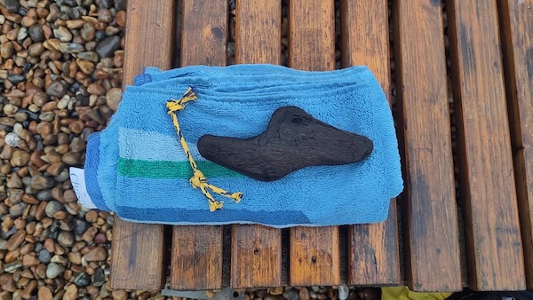 Some small driftwood and sea-worn plastic cord placed on a towel resting on a bench with sea pebbles in the background.
